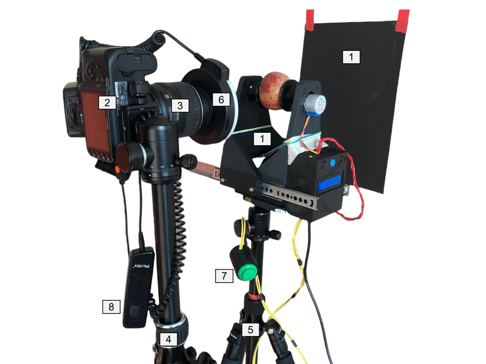 3D-printed black Apple Rotator Device clamping an apple with two stepper-motor-driven arms, mounted on a camera rail